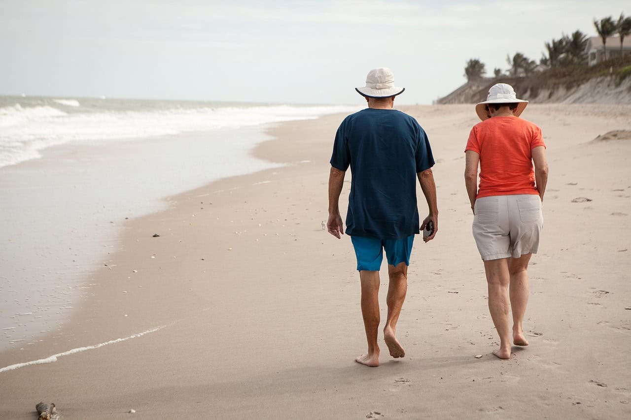 An older couple in sun hats walking along the beach
