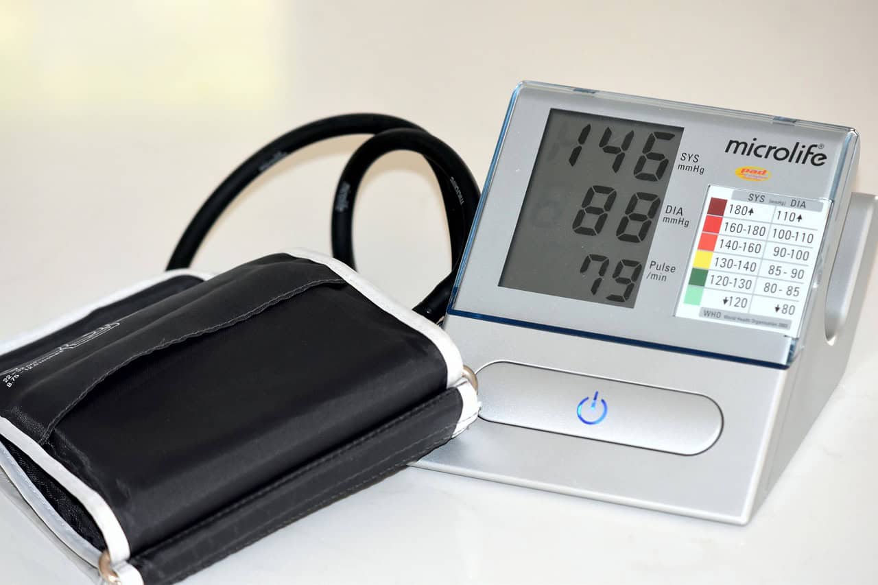 A home blood pressure monitor showing a reading, next to its arm cuff
