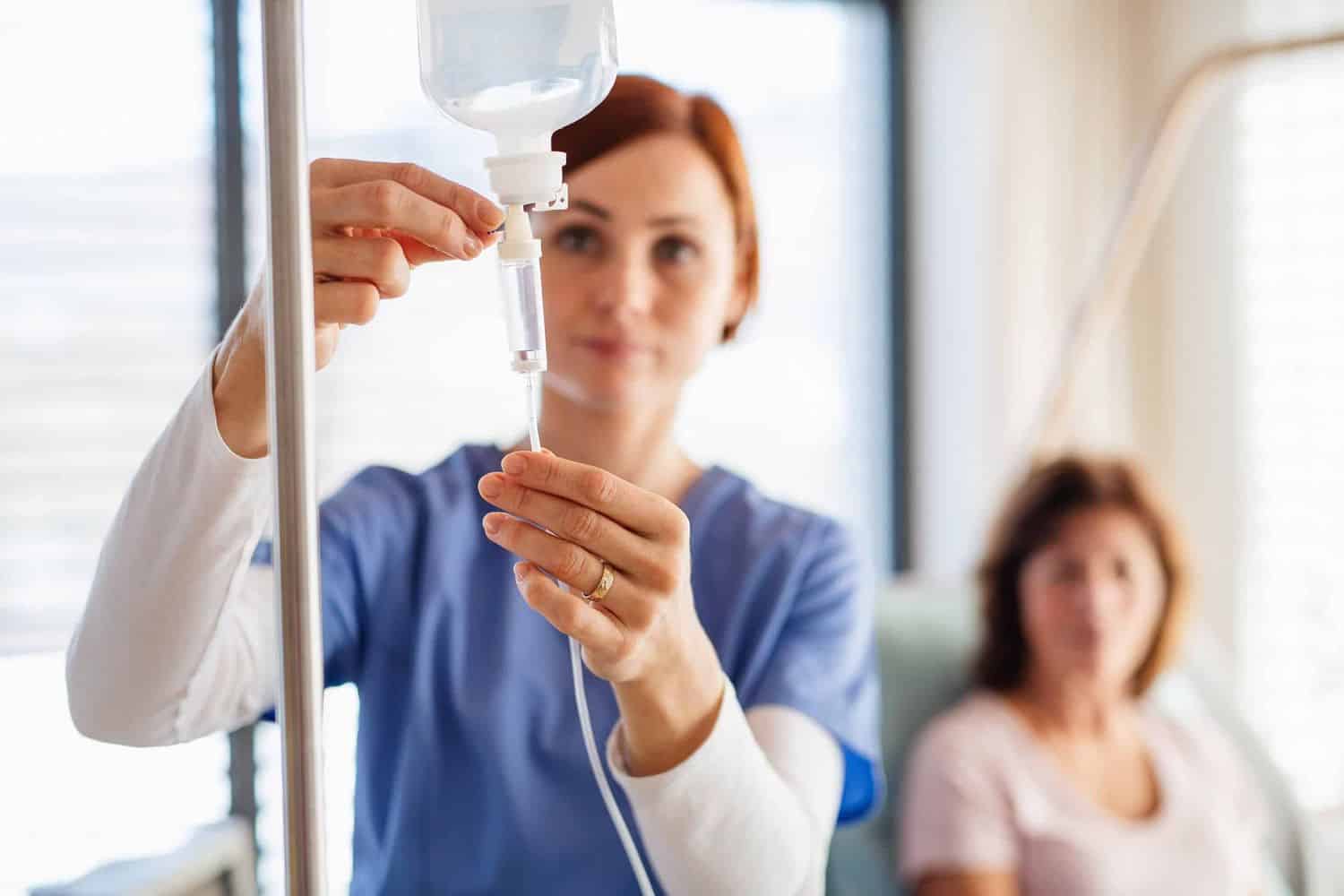 A nurse adjusting an IV bag with a patient relaxing nearby