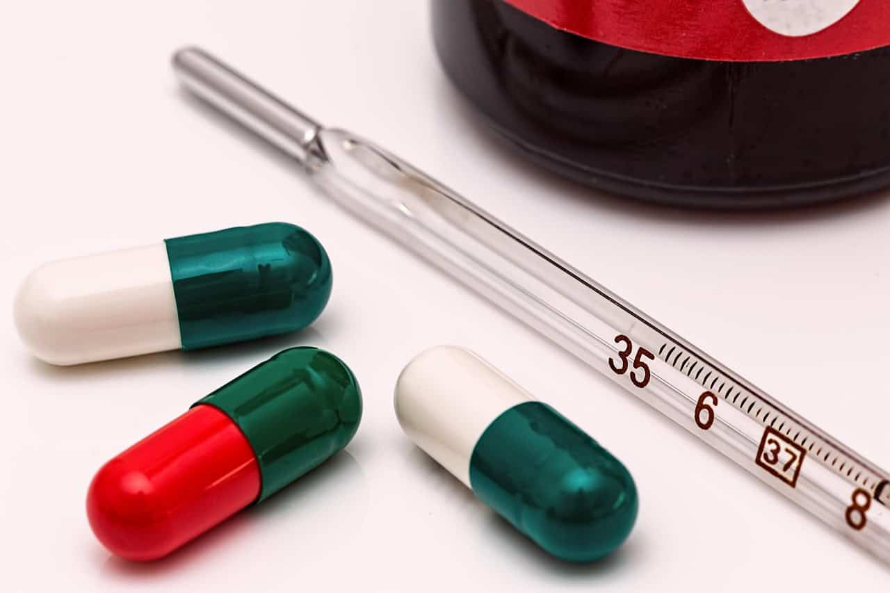 A thermometer next to cold medicine capsules