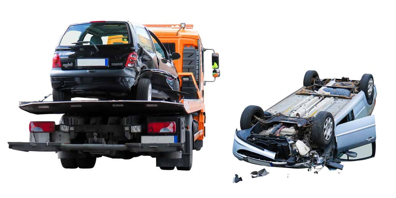 A tow truck carrying a car after an accident, with a damaged car beside it