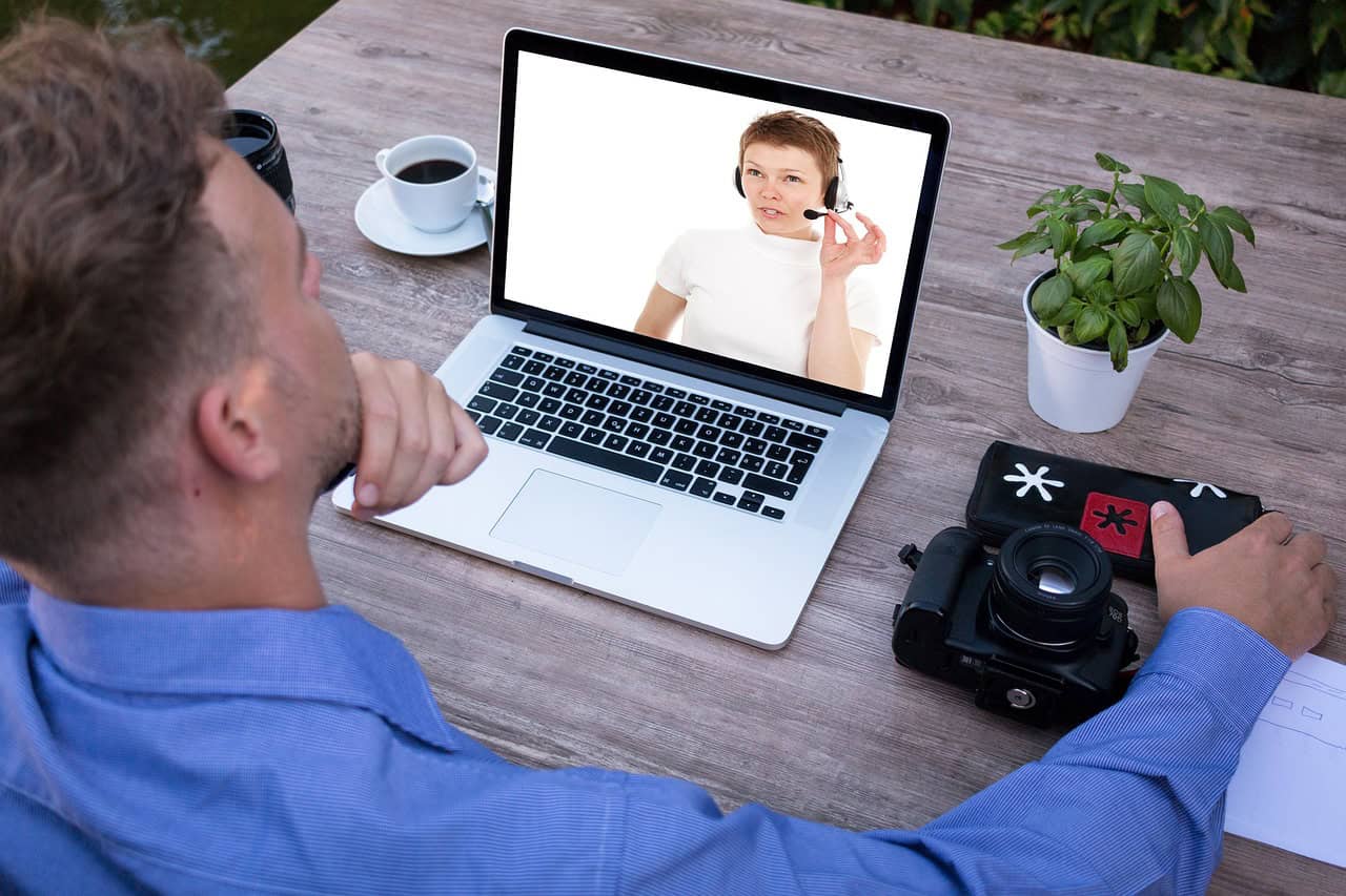 A man on a video call with a woman wearing a headset on his laptop screen